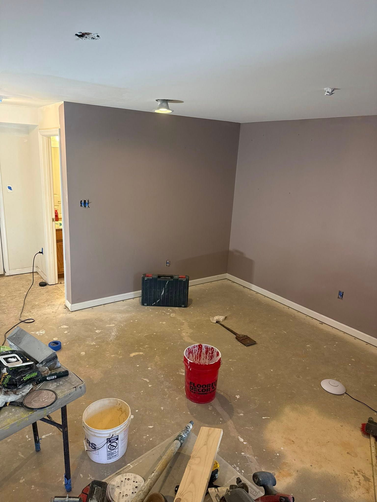 Room being renovated with taupe walls, paint splatters on floor, and tools.