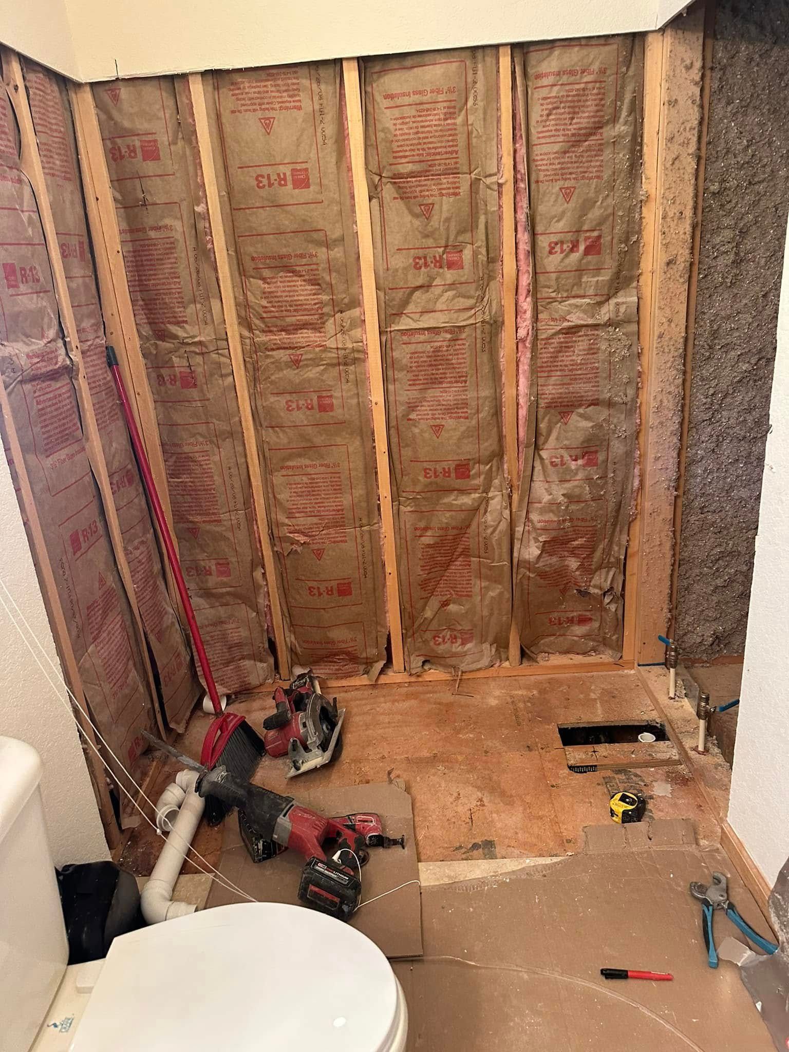 Bathroom renovation in progress, exposed studs, insulation, toilet, tools on floor.