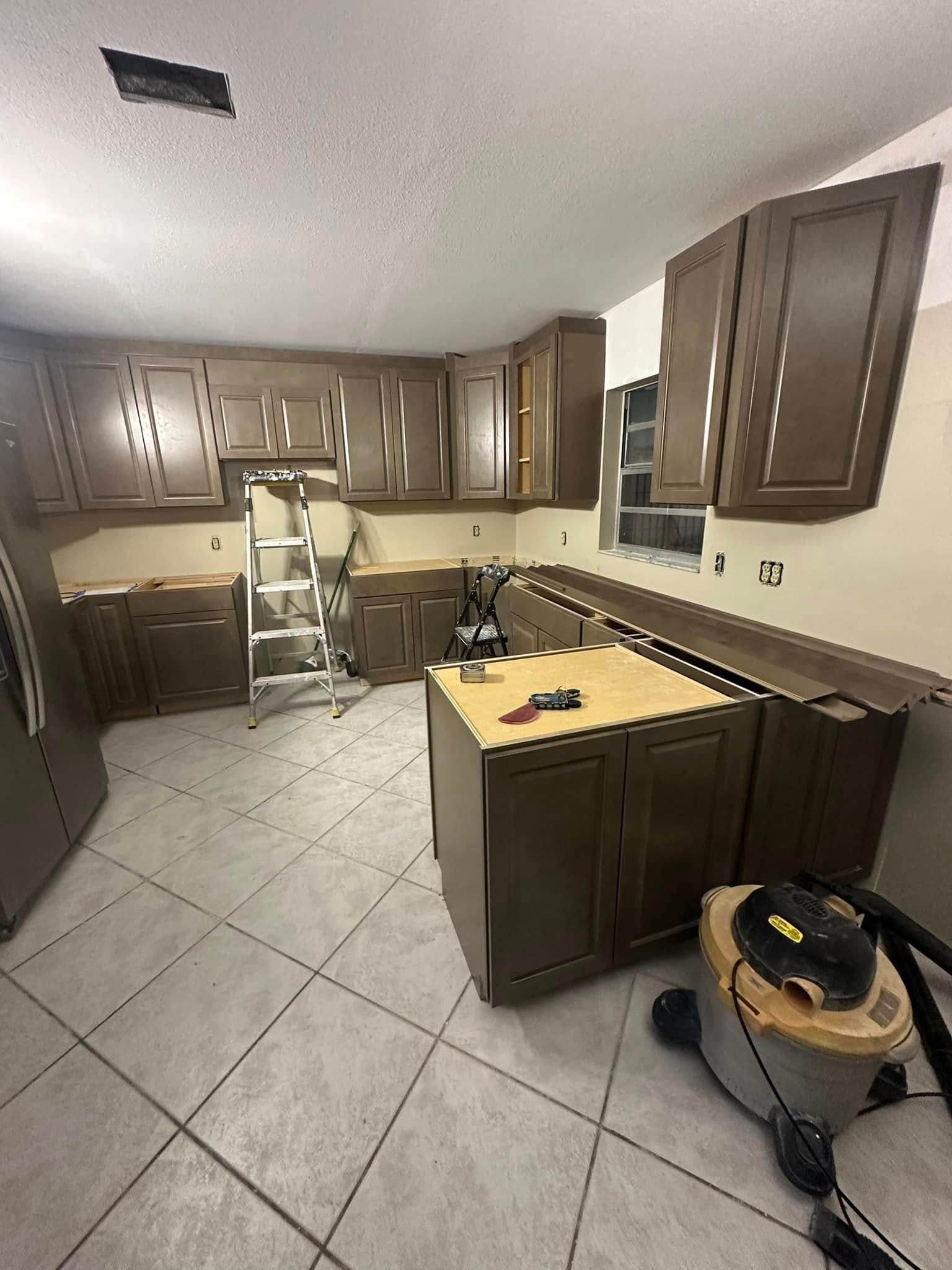 Kitchen remodel with brown cabinets and light countertops; a ladder and a vacuum are present.