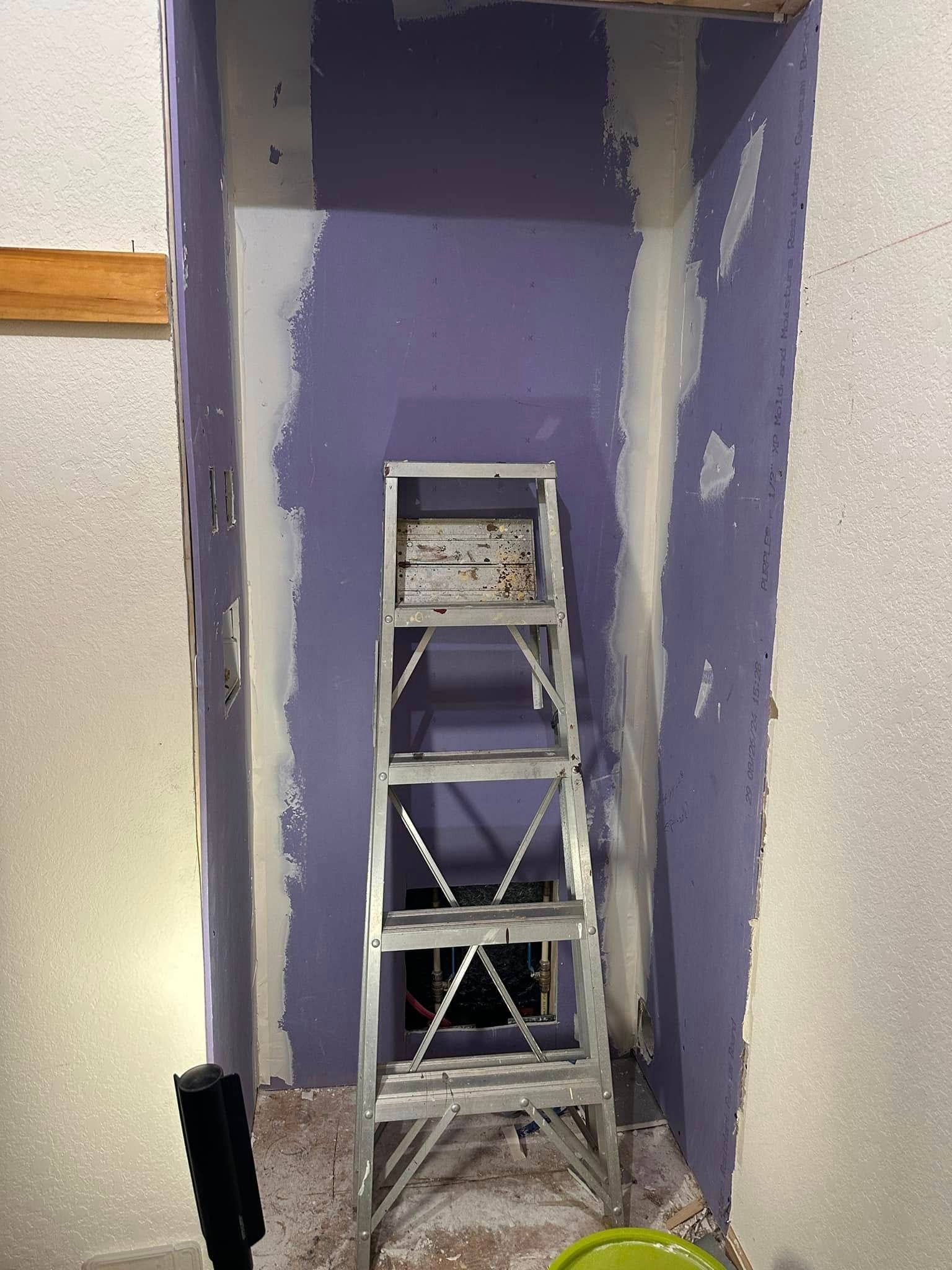 A step ladder inside a room under construction, with purple drywall and unfinished walls.