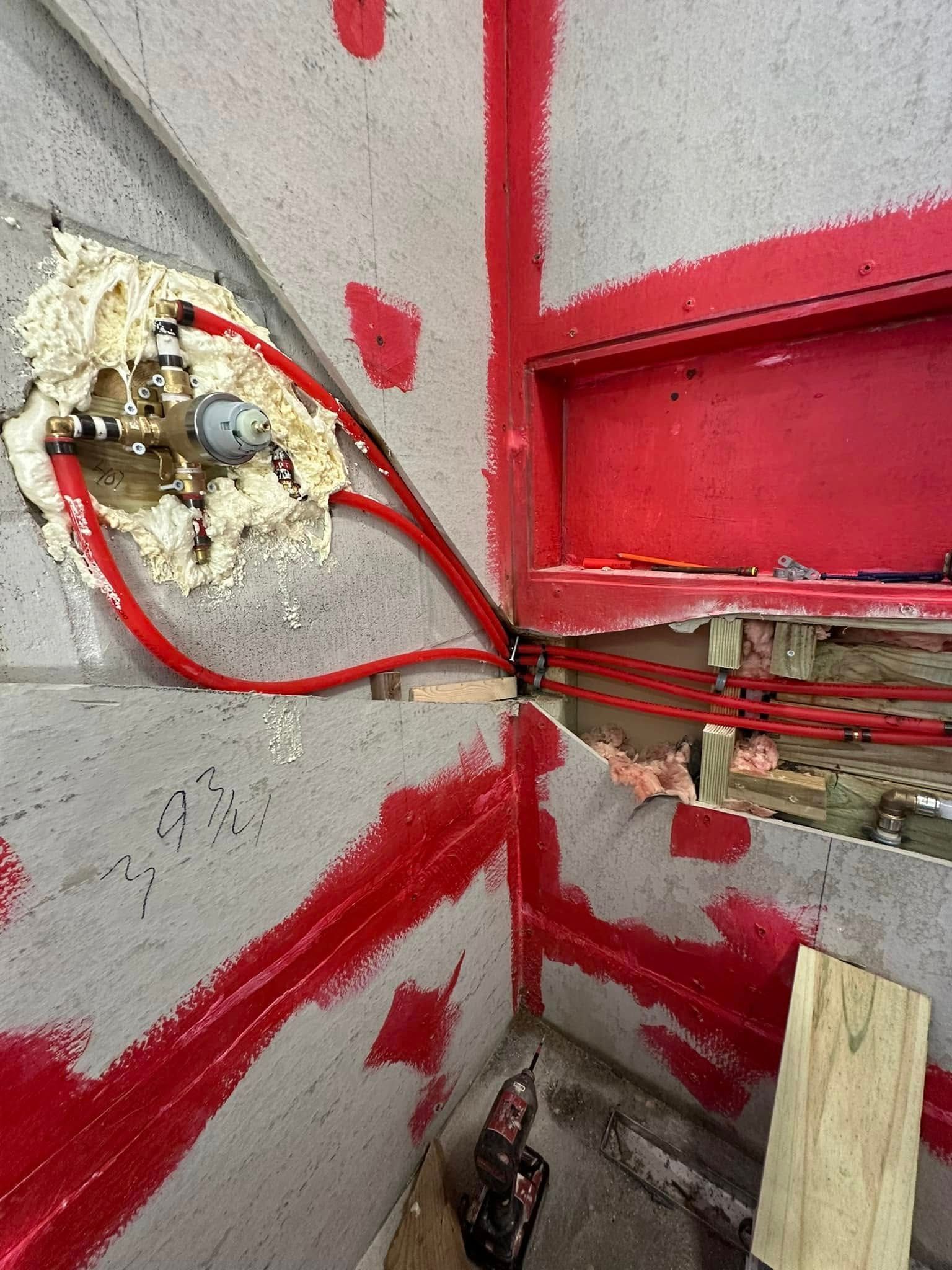 Plumbing pipes and fixtures surrounded by spray foam in a corner during construction, with red paint and a built-in niche.