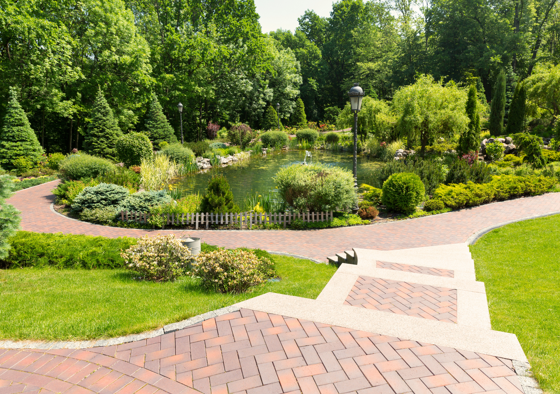 A brick walkway leading to a pond in a park