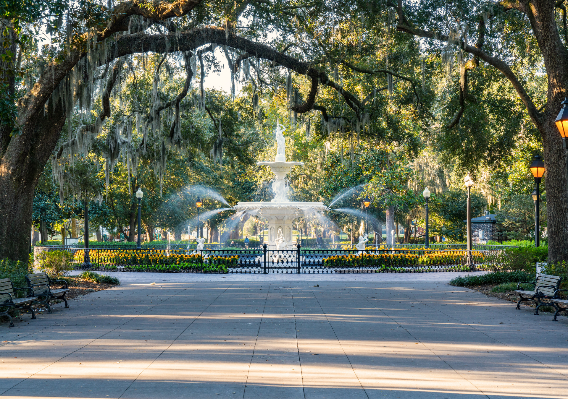 There is a fountain in the middle of a park surrounded by trees.