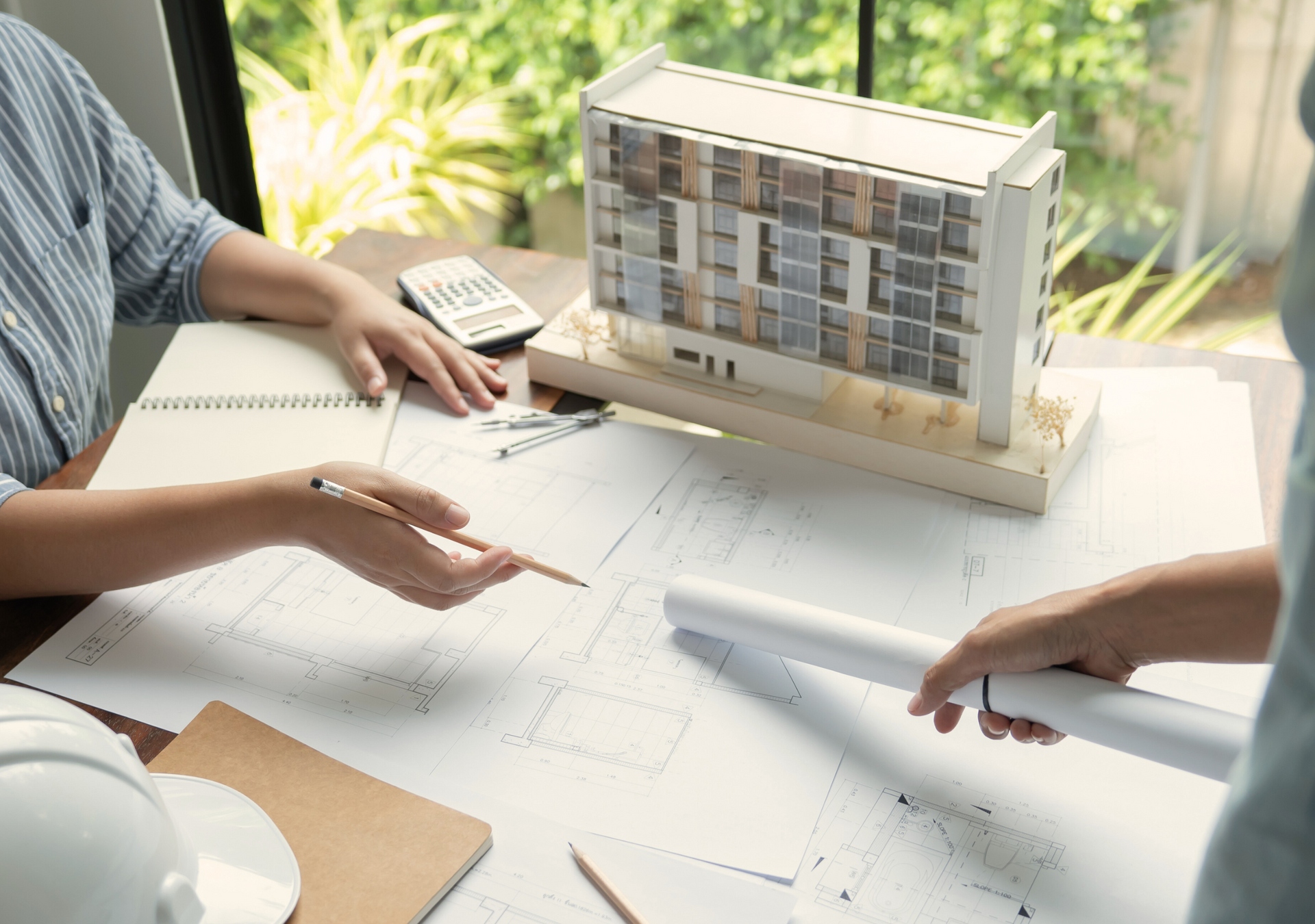 Two people are sitting at a table looking at a model of a building.