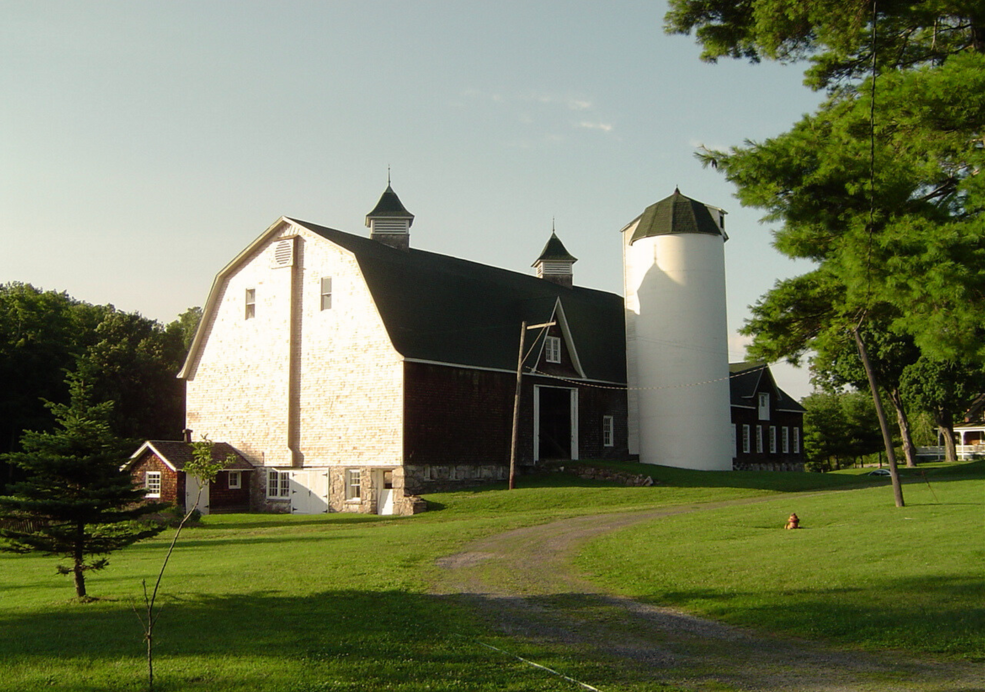 A large white barn with a silo in the background.