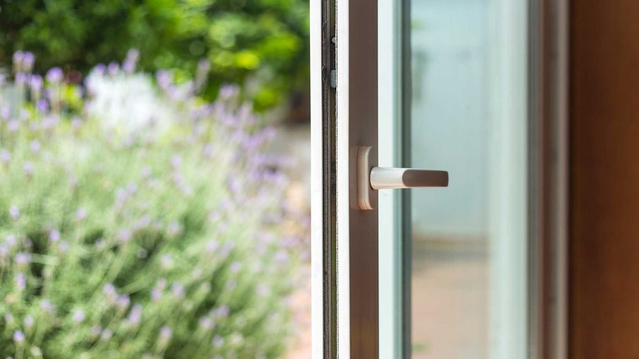 Partially open window with a silver handle, overlooking green foliage.