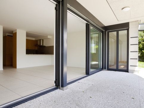 Glass sliding doors lead from a balcony into a modern, open-concept living space with a kitchen.