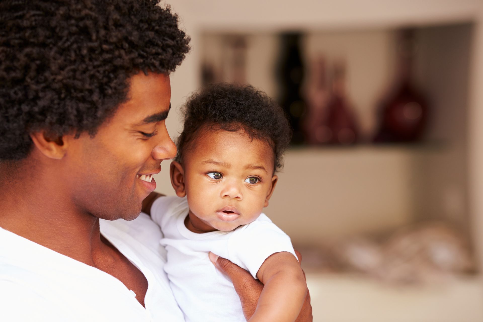 Man smiles, holding a baby in a white onesie.