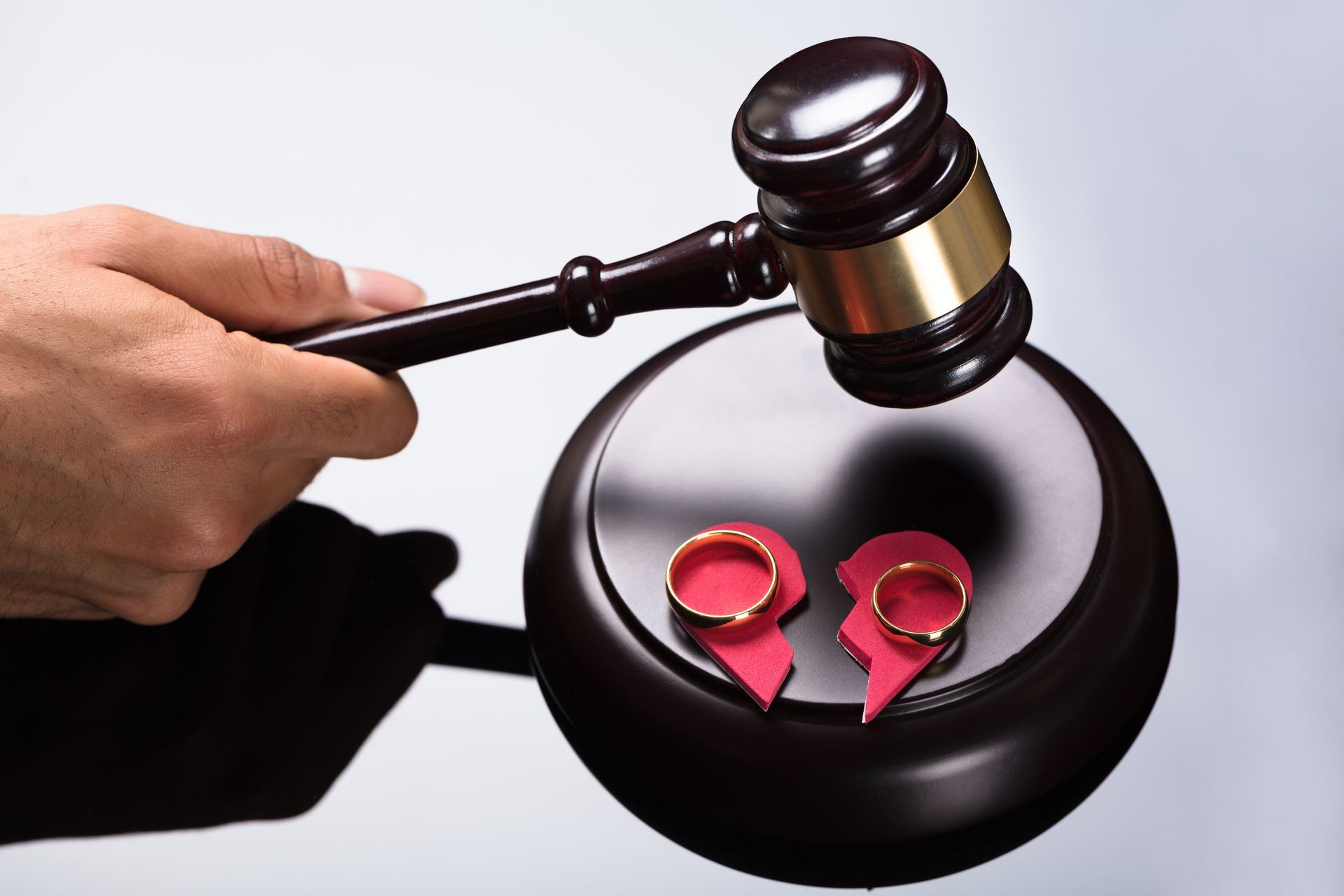 Gavel striking a wooden block with two broken rings on it, symbolizing divorce.