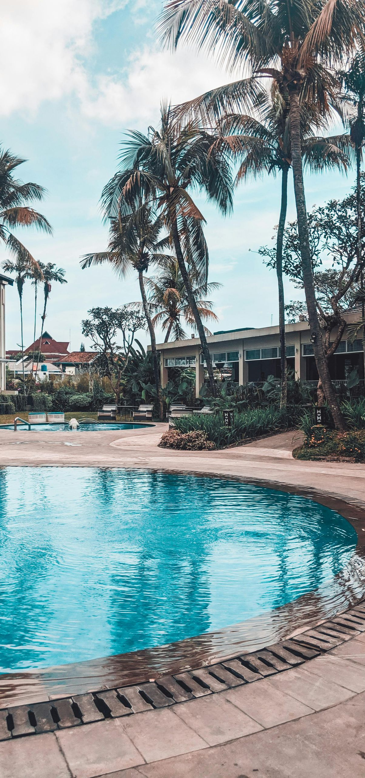 A pool with clear blue water surrounded by palm trees and a building on a sunny day.
