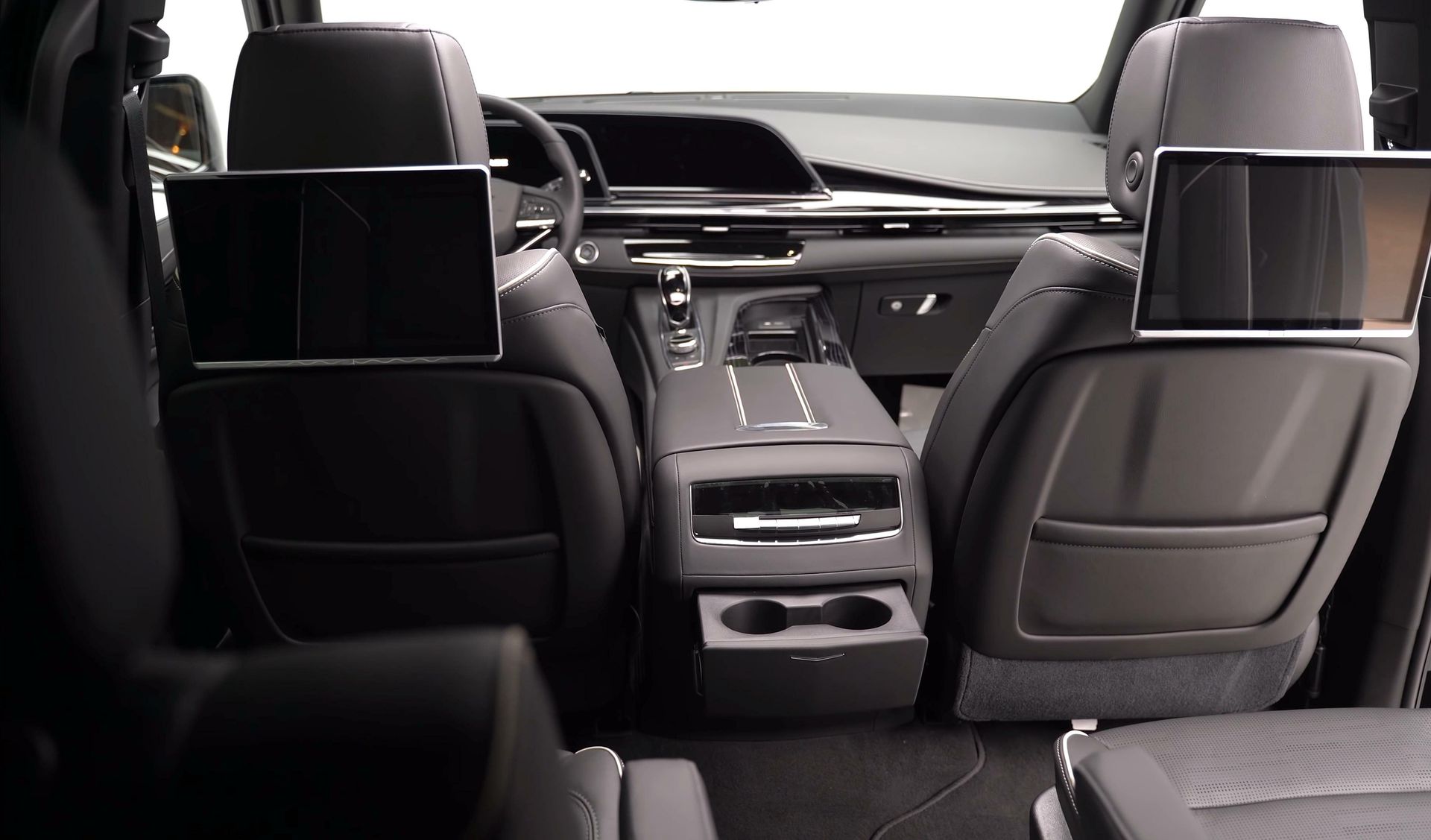 Back interior of a car with two rear seats, each with a screen. Black and gray color scheme.