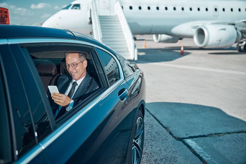 Man in suit looking at phone, exiting car near airplane on tarmac.