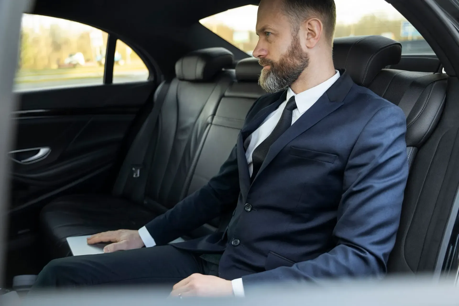 Man in suit sitting in the back seat of a car, looking out the window.
