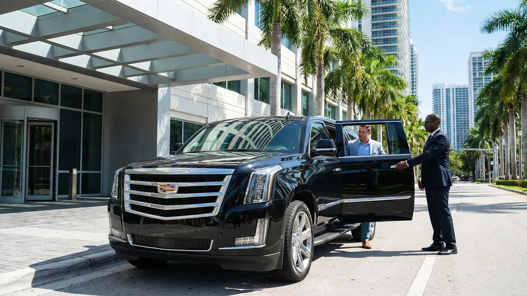 Black SUV at hotel entrance, driver opening door for passenger. Sunny day.