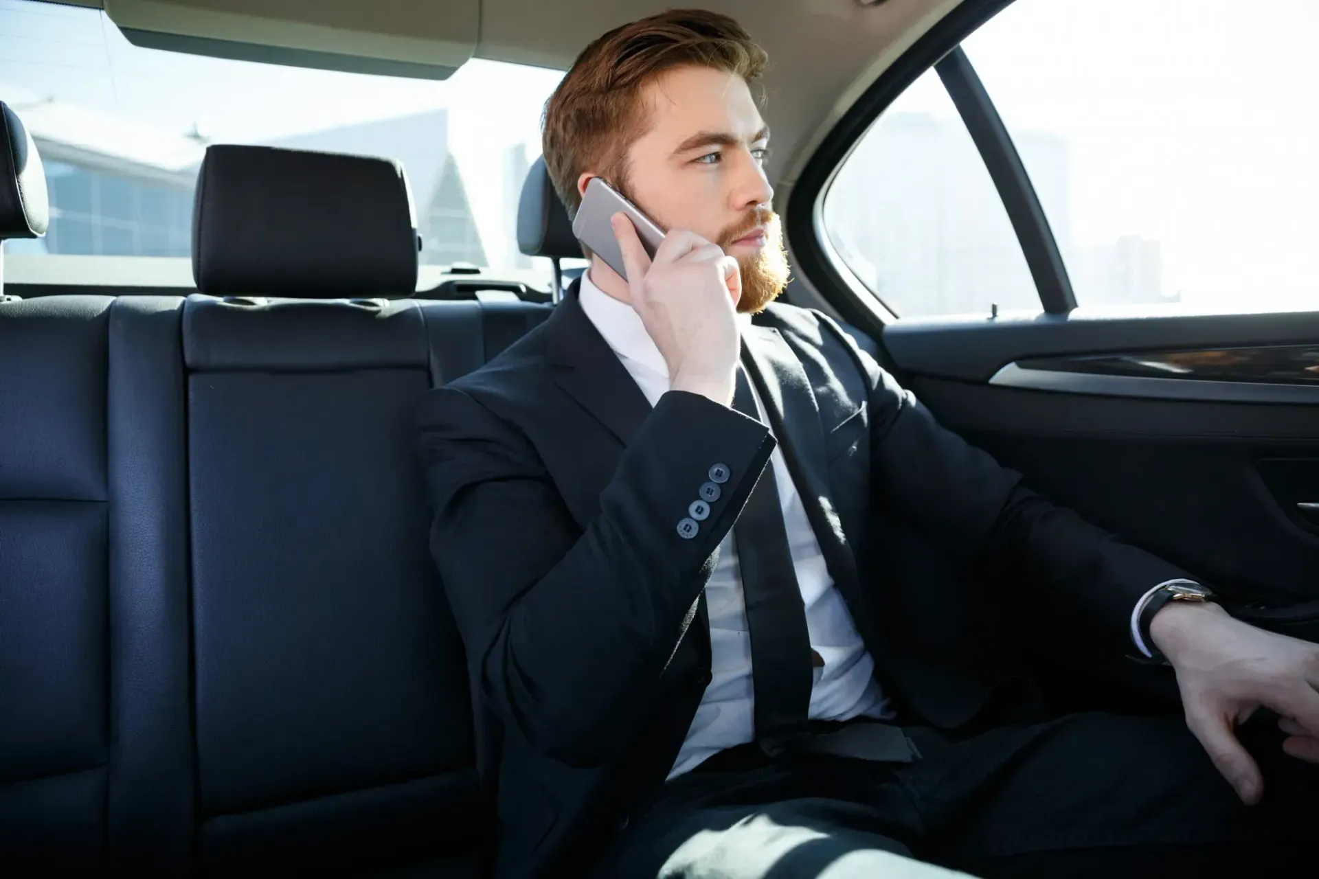 Man in a suit talking on the phone in the back seat of a car.