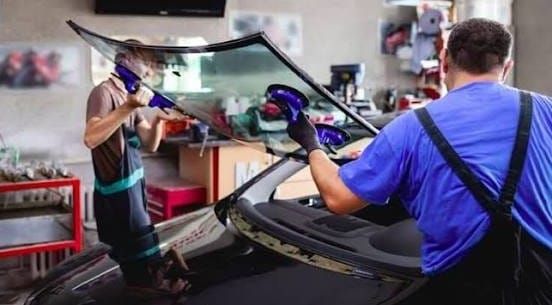 Dos trabajadores del sector automotriz instalando un parabrisas en un taller mecánico.