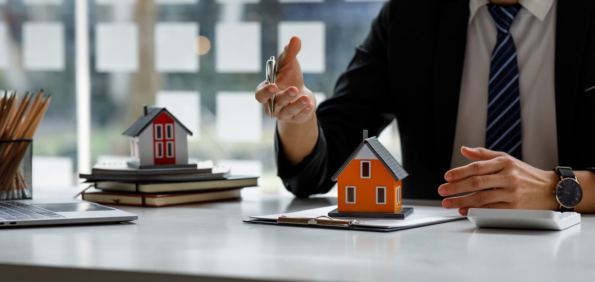 A Man in a Suit and Tie is Sitting at a Desk With Two Small Houses on It