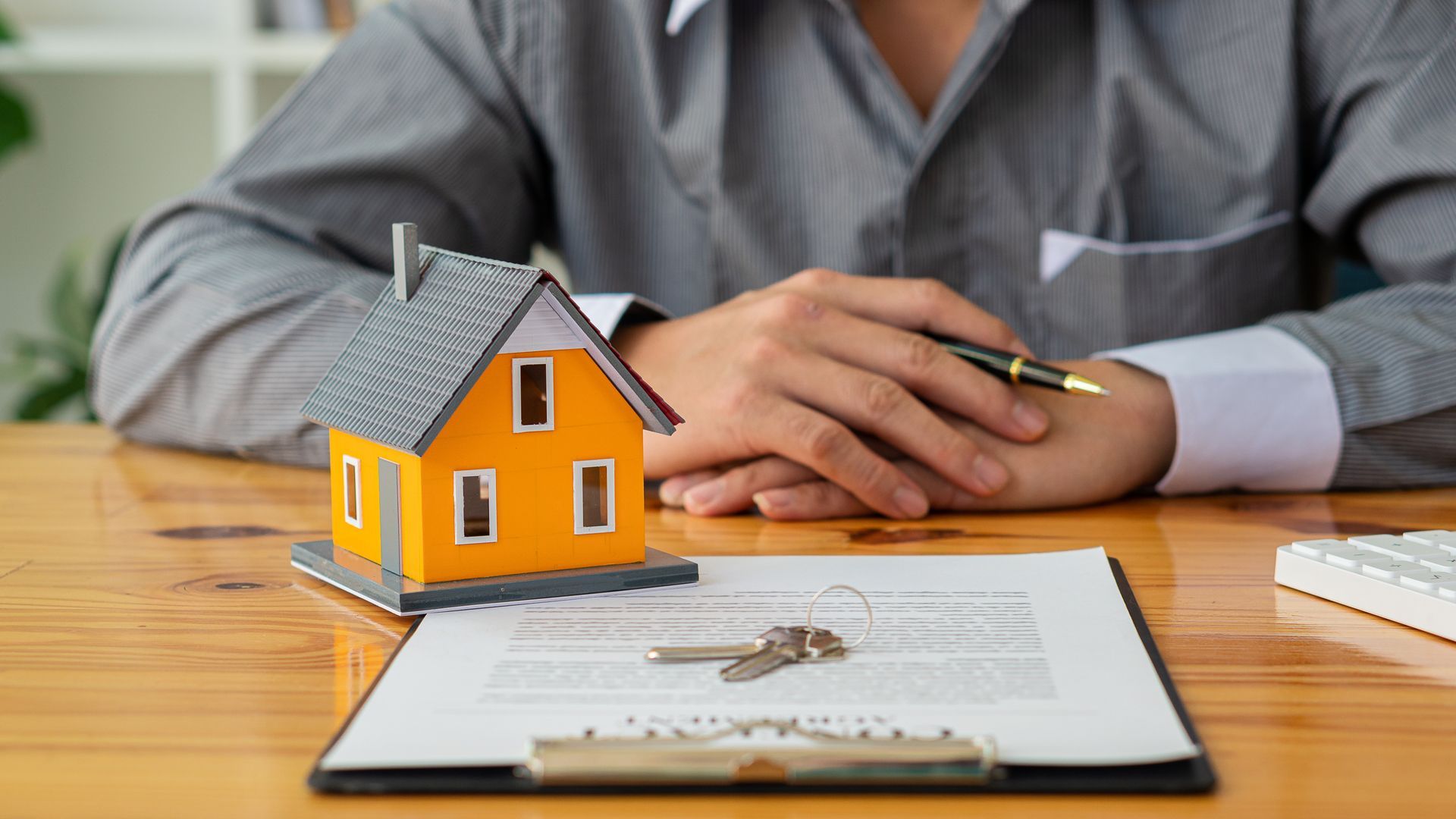 A Man is Sitting at a Table With a Model House and Keys