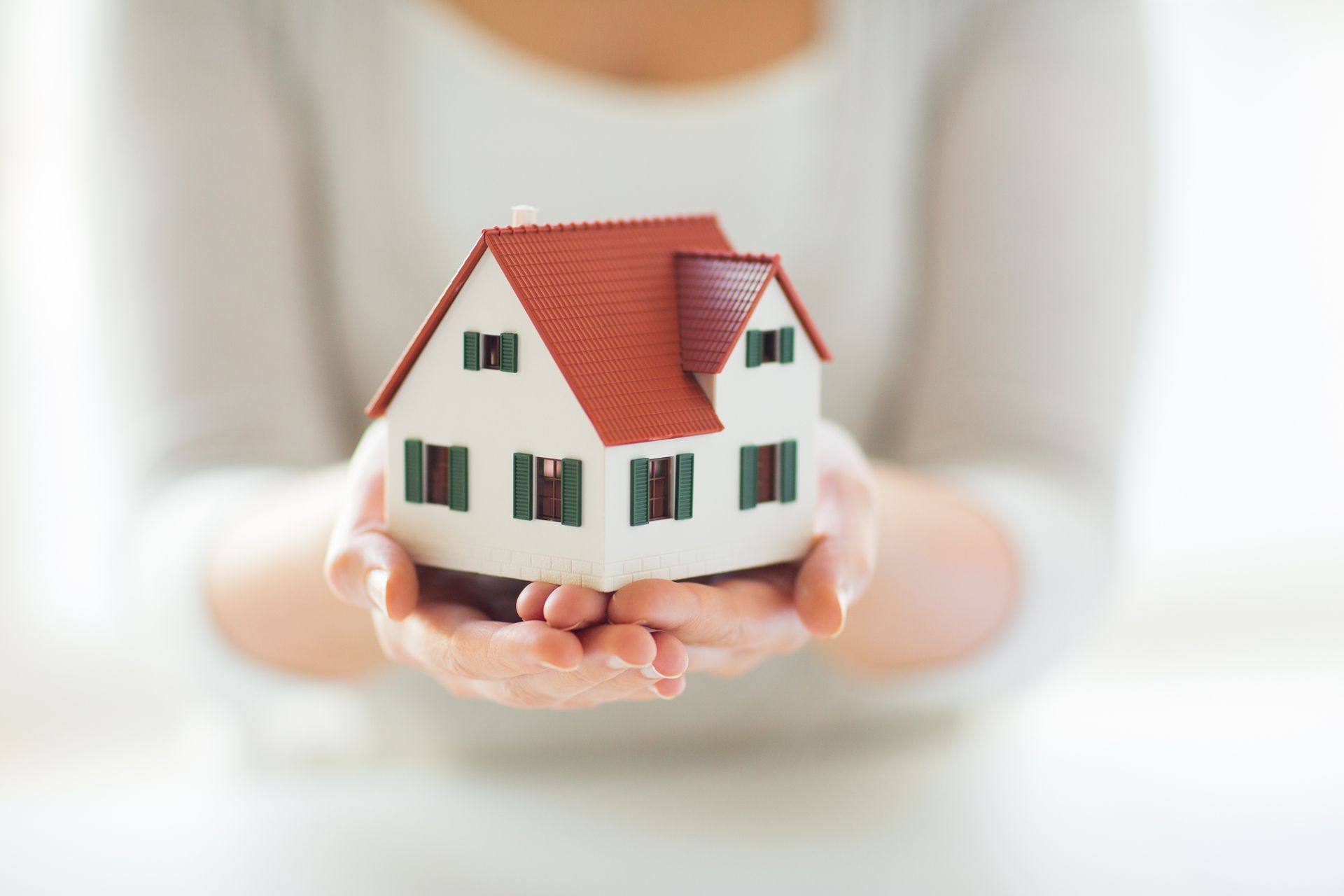 A Woman is Holding a Small Model House in Her Hands