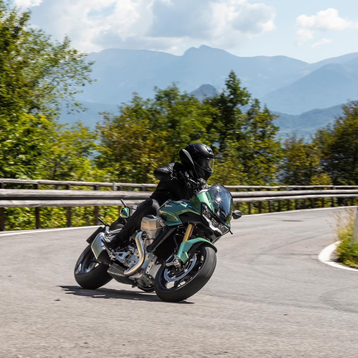 Una persona sta guidando una motocicletta verde lungo una strada con le montagne sullo sfondo
