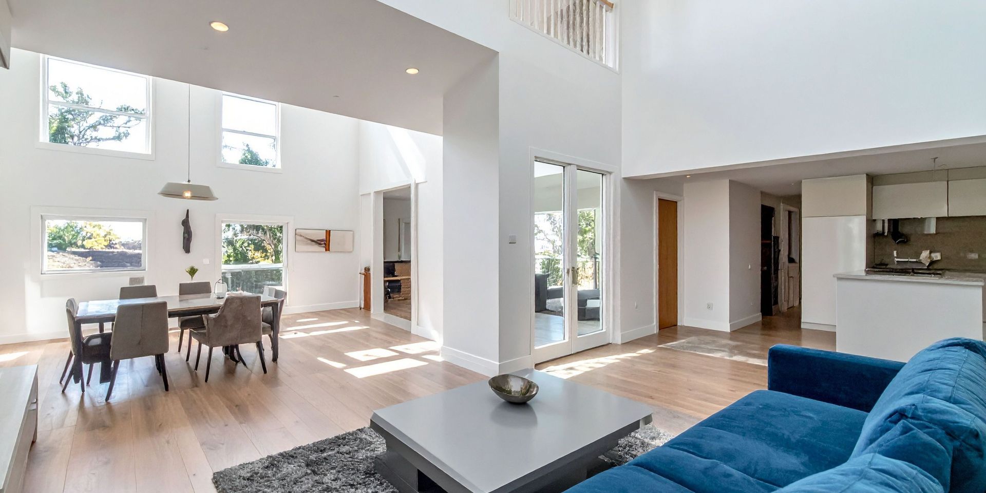 Bright, open-plan living room with high ceilings, dining area, blue sofa, and natural light.