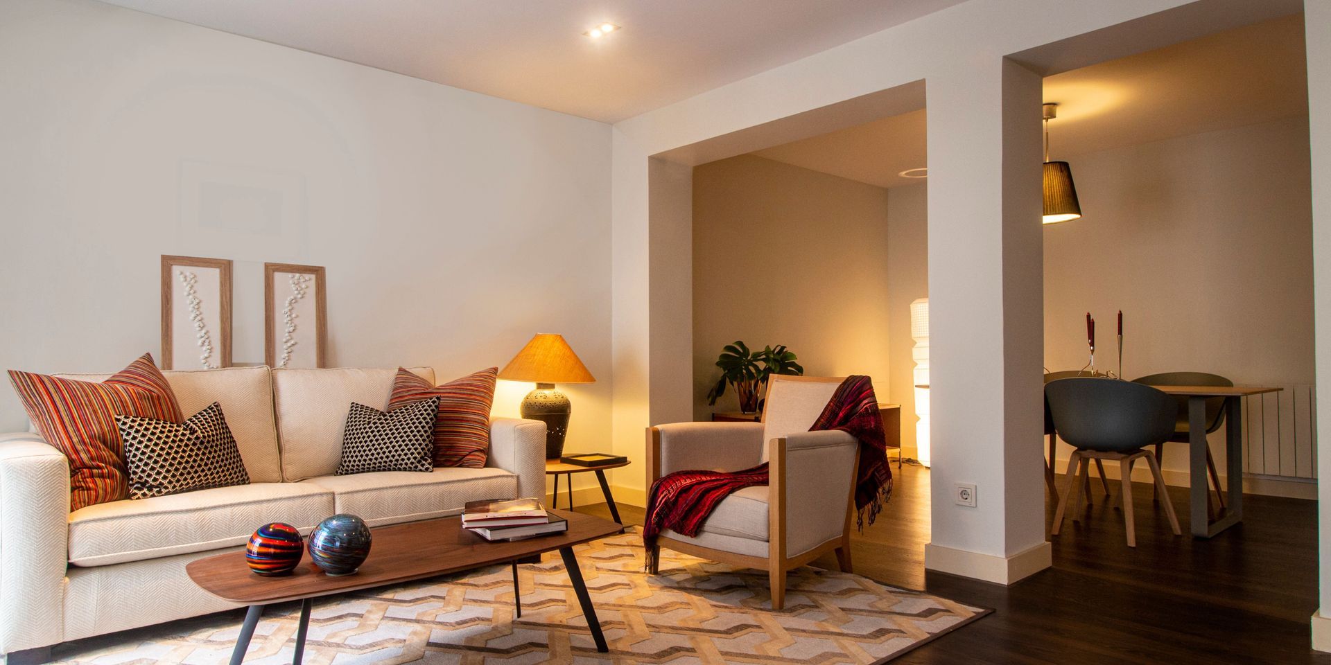 Living room with a cream sofa, wooden coffee table, and cozy armchair. Adjacent dining area visible.