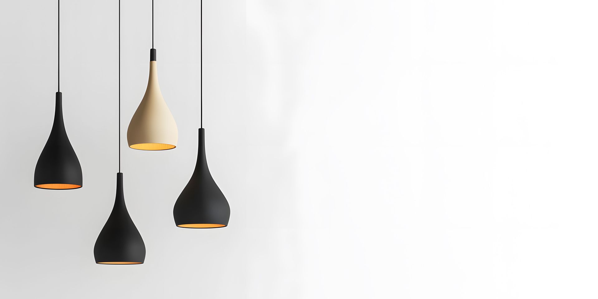 Four pendant lights hanging from the ceiling, three black and one beige, against a white wall.