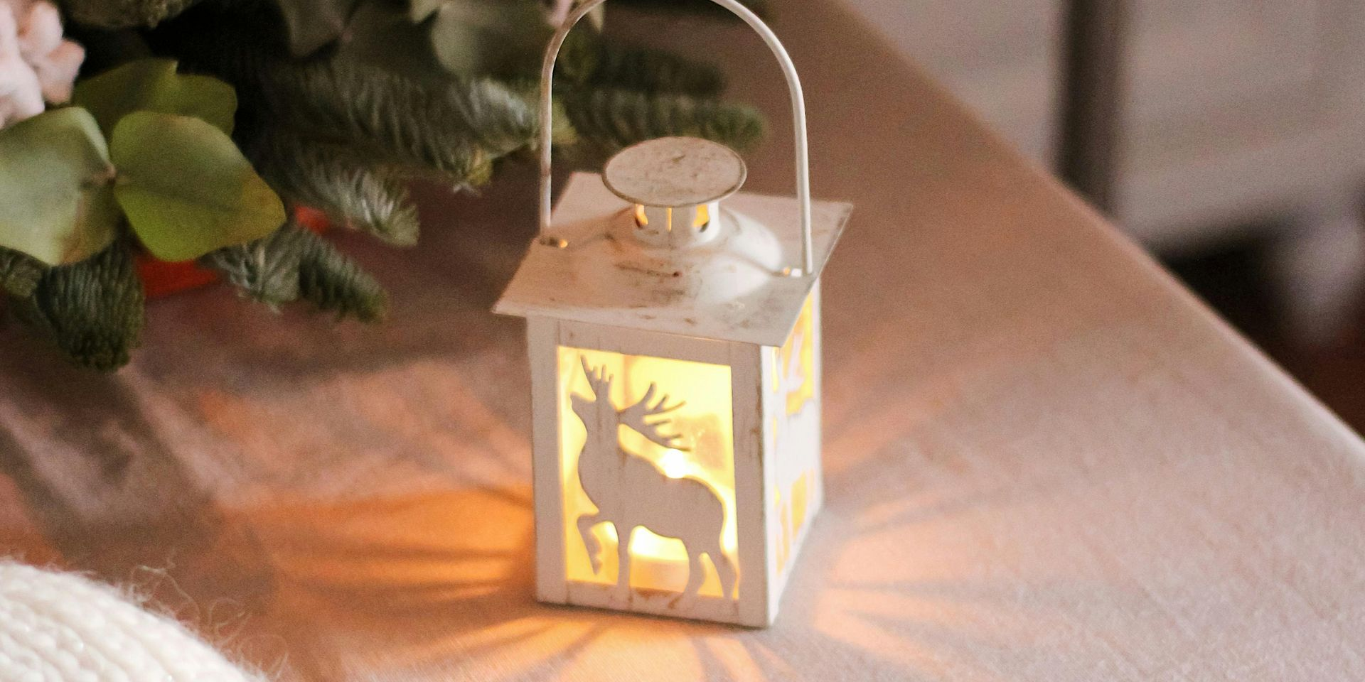 White lantern with a deer silhouette, lit from within, on a white table. Floral arrangement in background.