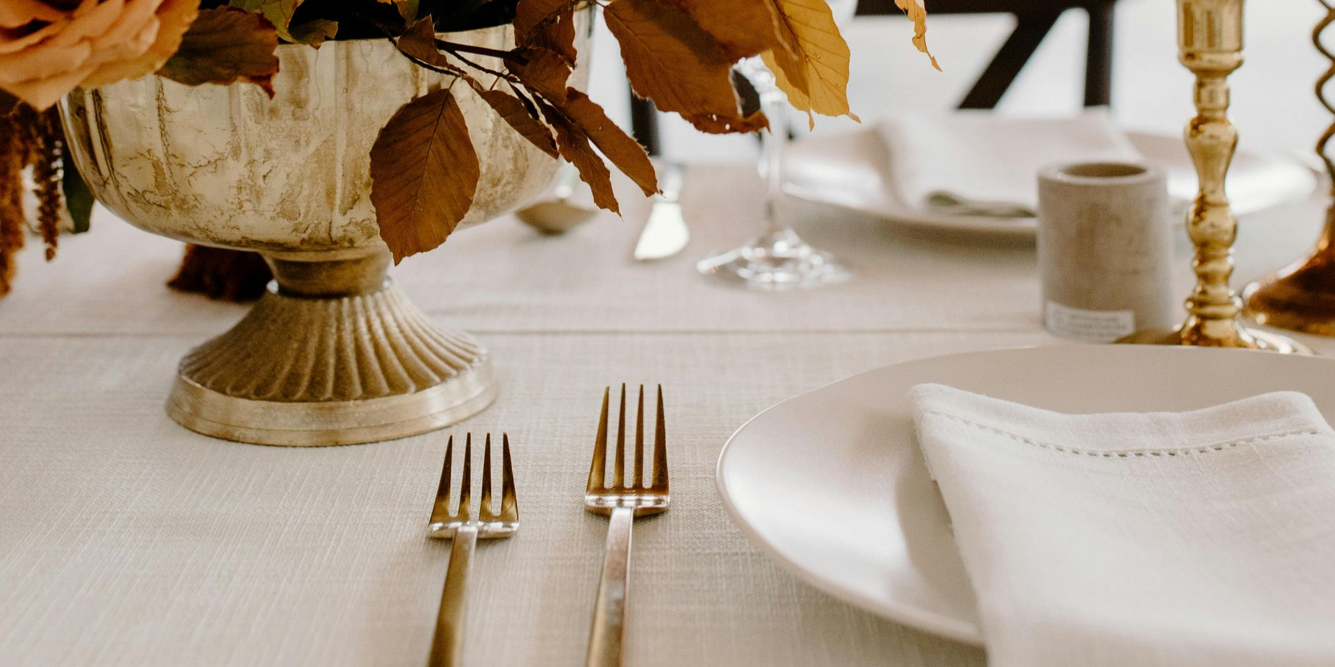 Table setting with gold forks, white plate and napkin, floral centerpiece.