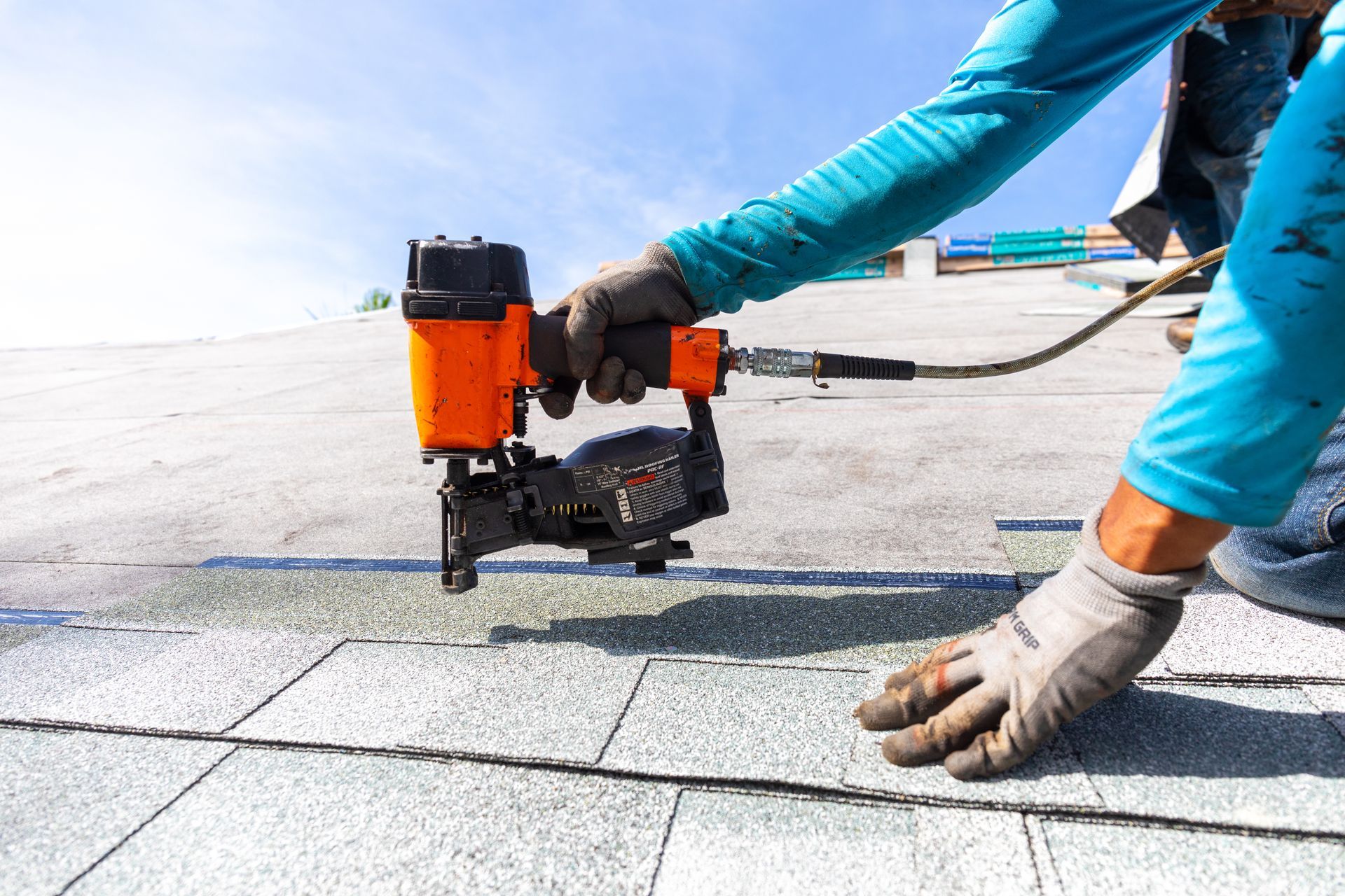Close-up of a roofer, performing roofing services, installing roof shingles with a nail gun.