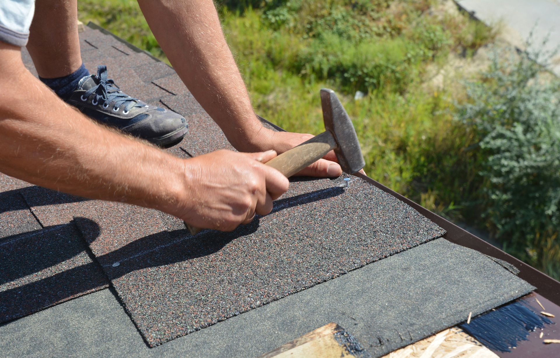 Person hammering shingles onto a roof; close-up view.