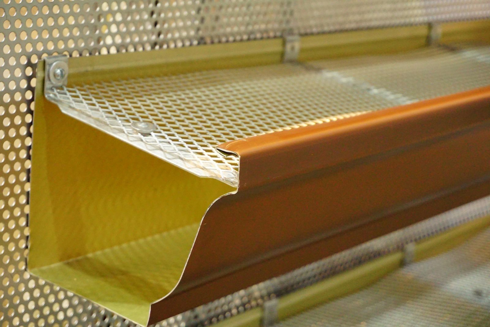 Brown gutter with a yellow metal mesh screen to prevent debris from clogging.