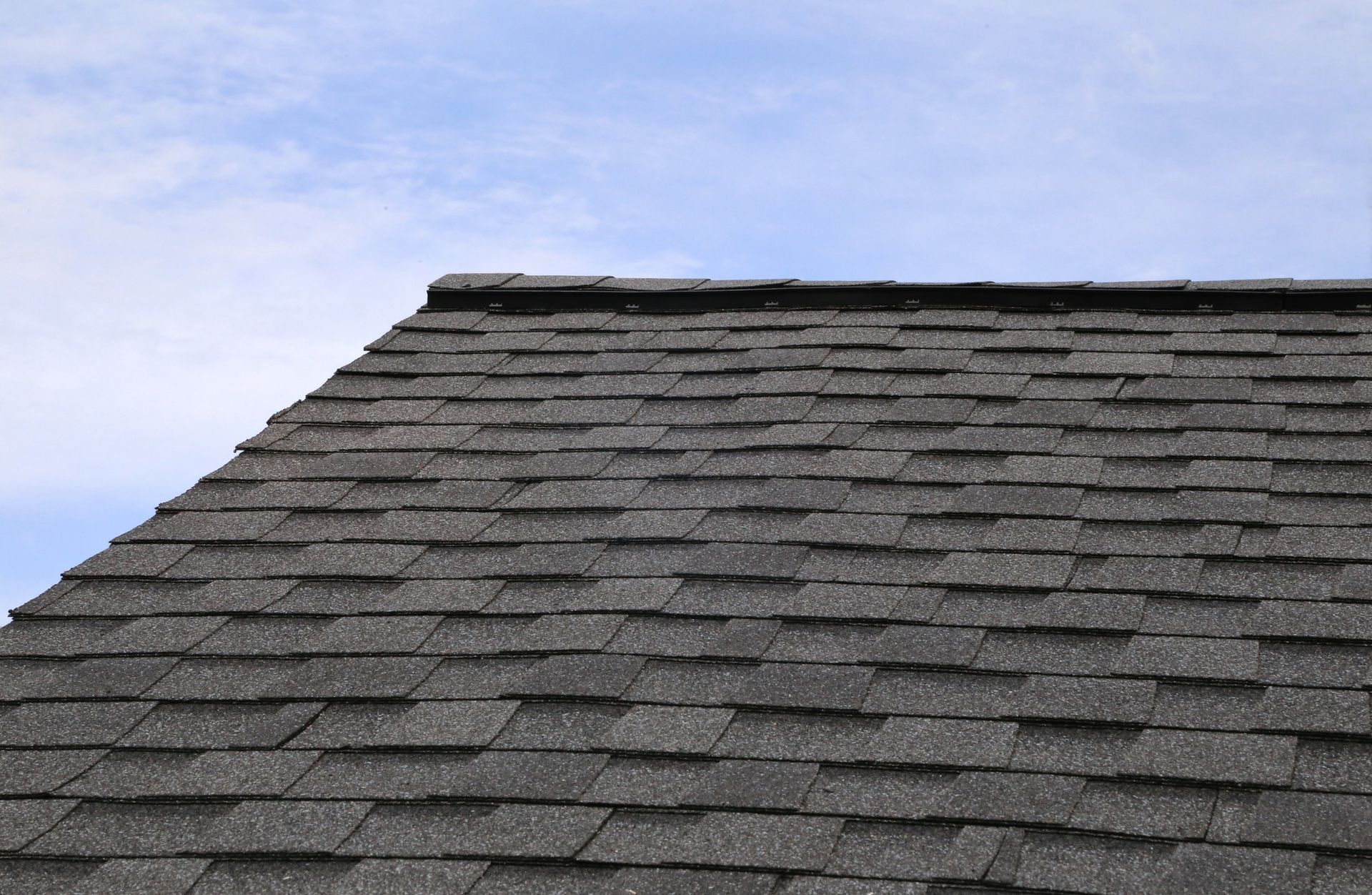 Dark gray asphalt shingle roof against a blue sky with wispy clouds.