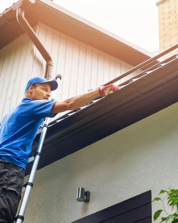 A man is standing on a ladder cleaning the gutters of a house.