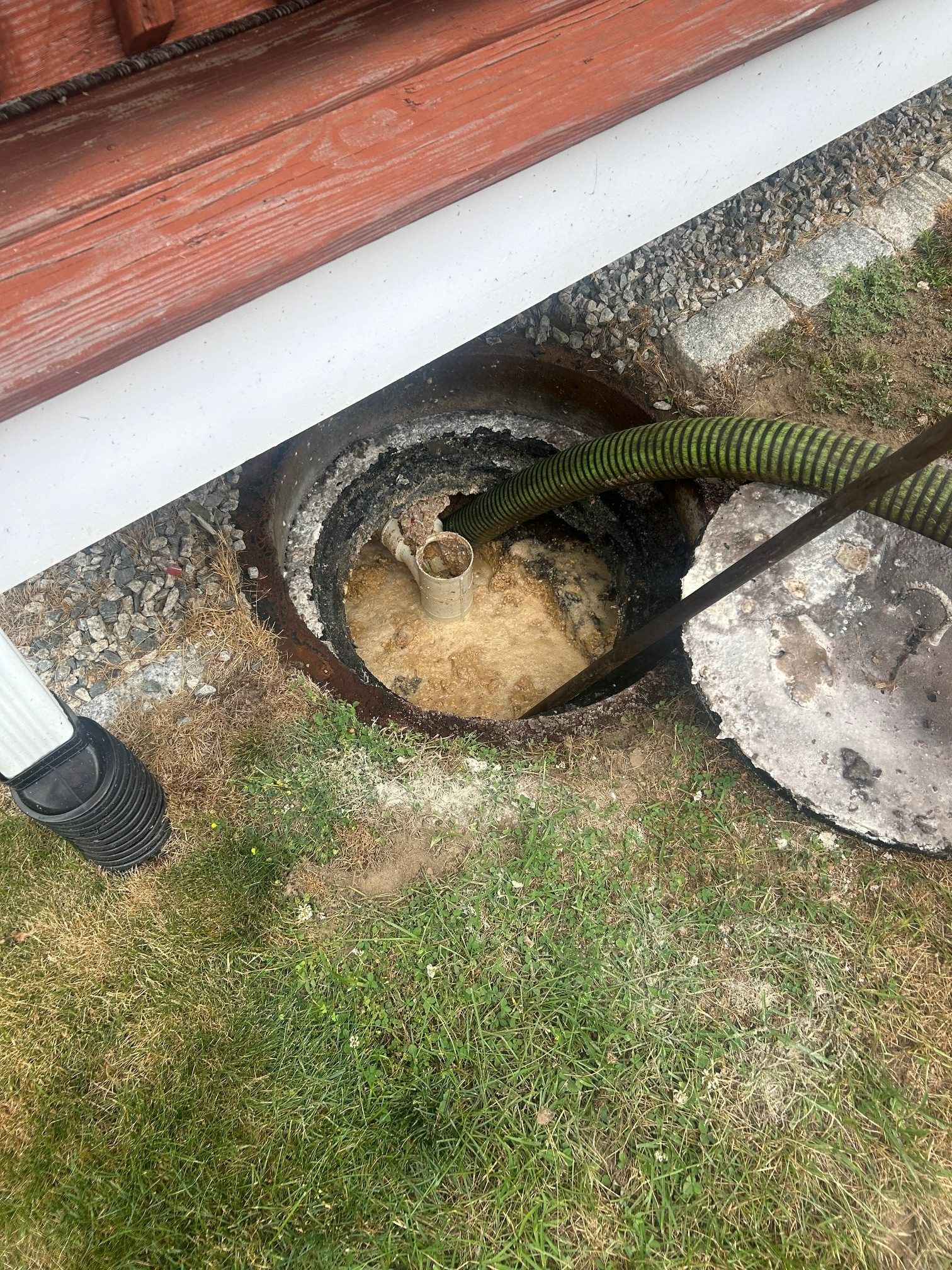 Septic tank being pumped; green hose, brown structure, grass, and a white gutter.