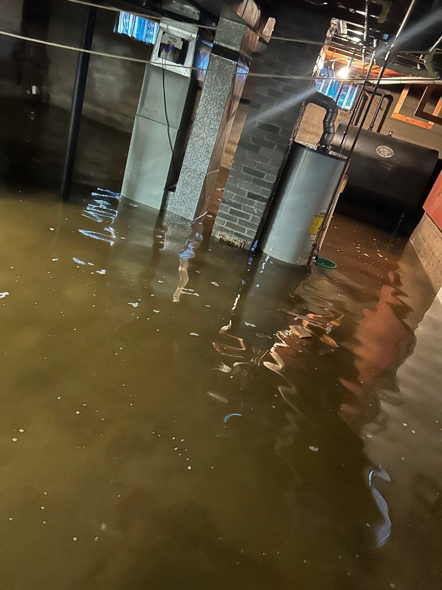 Flooded basement with appliances and water up to knee level; a dark, interior shot.