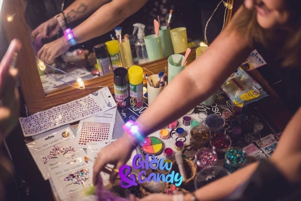 Personas en una mesa de trabajo con pulseras que brillan en la oscuridad, pintura y brillantina.