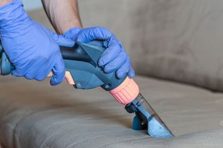 A Person Wearing Blue Gloves Is Cleaning A Couch With A Vacuum Cleaner — Experienced Cleaner in Bowen, QLD
