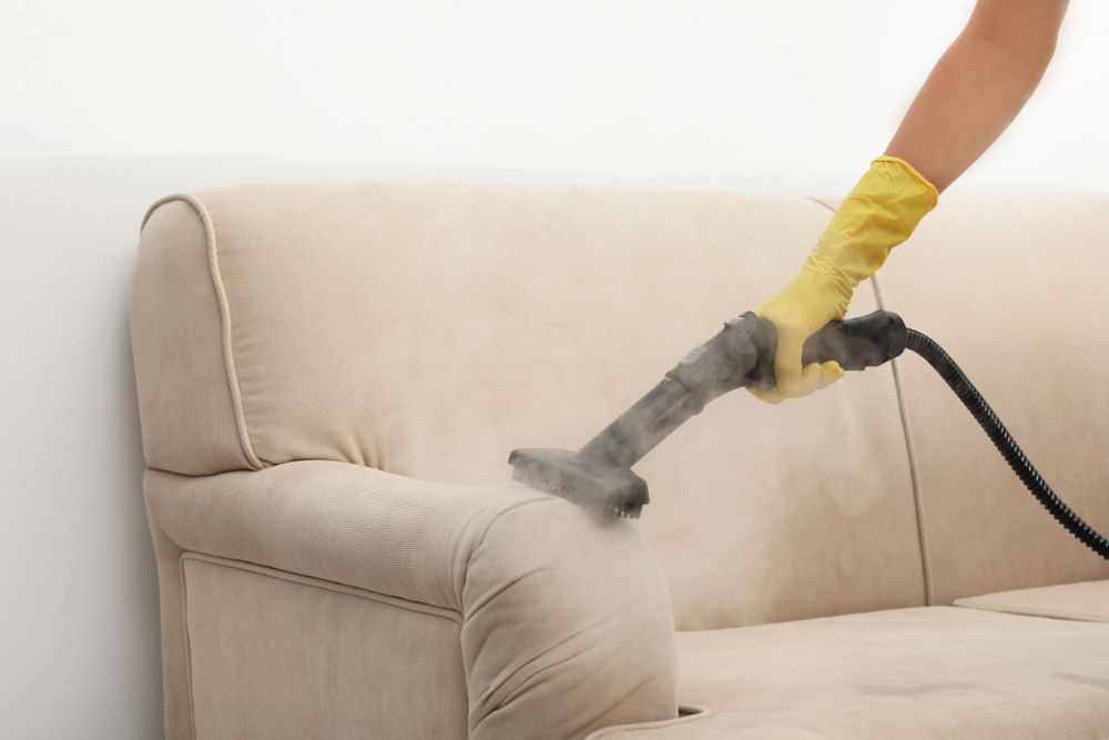 A Woman Removing Dirt From Sofa With Steam Cleaner In Living Room — Experienced Cleaner in Airlie Beach, QLD