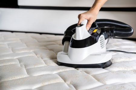 A Person Is Cleaning A Mattress With A Vacuum Cleaner — Big Red Carpet & Property Maintenance In Bowen, QLD