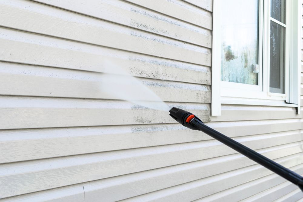 A Person Is Cleaning The Side Of A House With A High Pressure Washer — Big Red Carpet & Property Maintenance In Bowen, QLD