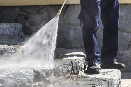 A Person Is Cleaning A Stone Wall With A High Pressure Washer — Big Red Carpet & Property Maintenance In Bowen, QLD