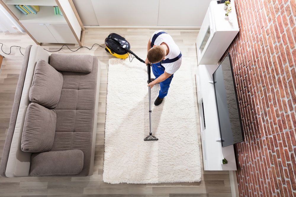 Male Worker Using Vacuum To Clean Carpets In A Home — Big Red Carpet & Property Maintenance In Bowen, QLD