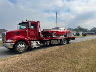 Red tow truck transporting a red classic car on a residential street.
