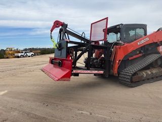 Red and black stump grinder attachment on an orange Kubota track loader on a dirt surface.