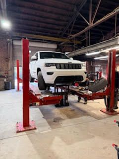 White SUV on a red car lift inside an auto repair shop.