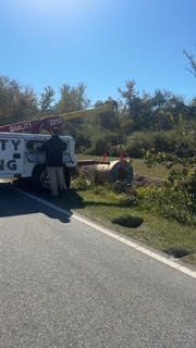 Truck with extended arm lifting an object near a roadside, person standing by the truck.