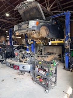 Truck on a lift in a garage with engine and tools on a cart.