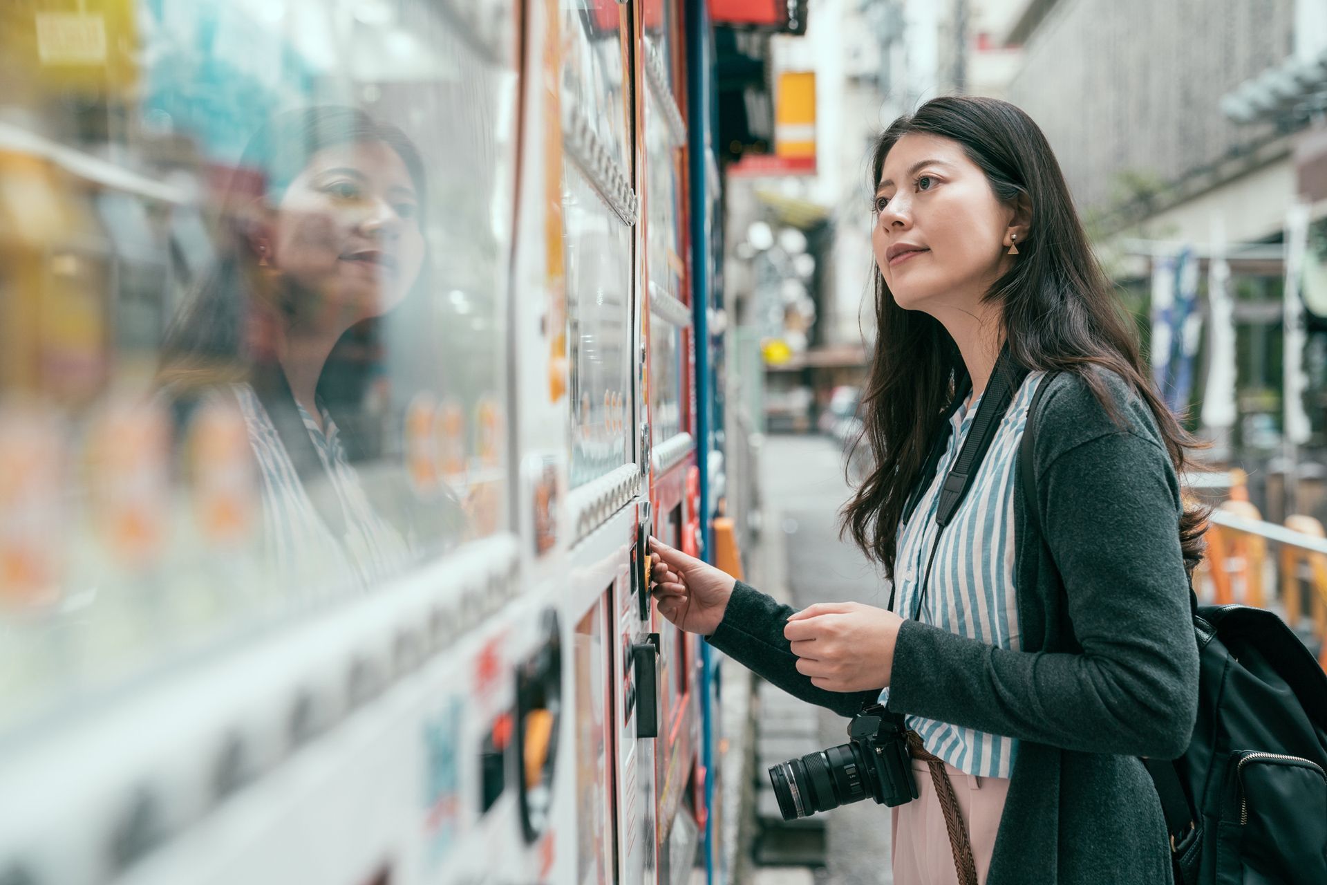 Woman inserting money into a vending machine on a city street.