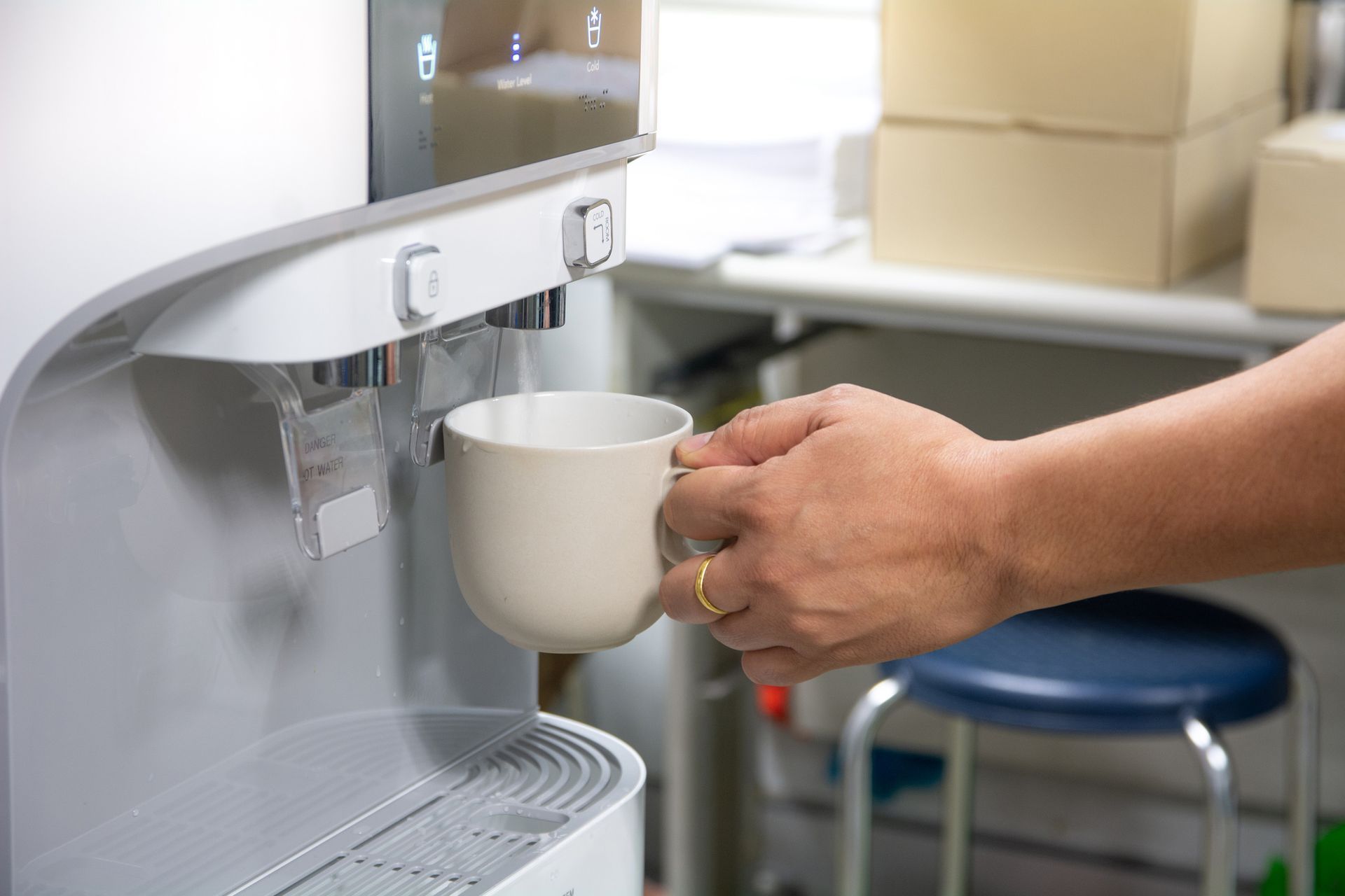 Hand filling a mug from a water dispenser in an office setting.